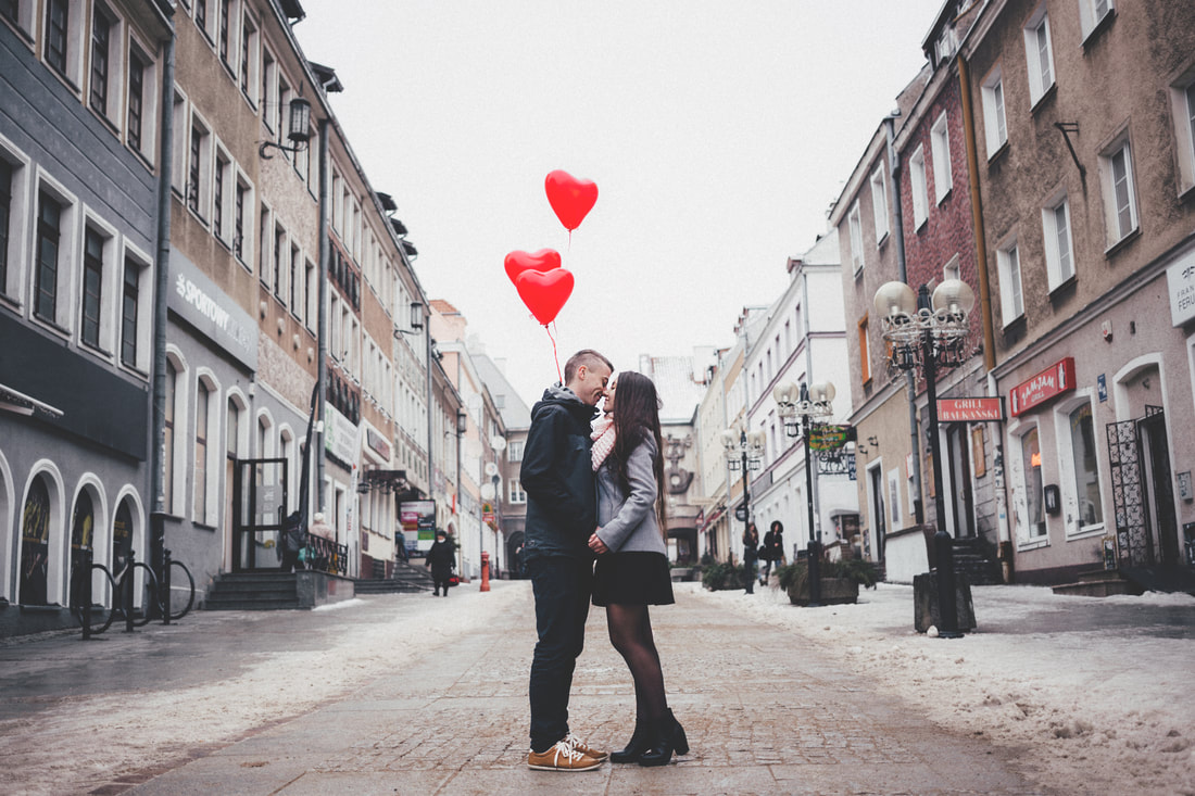man and woman kissing in street with heart balloons